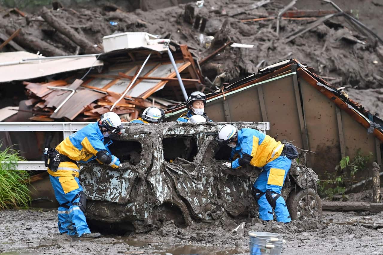 Rescuers check a damaged vehicle at the site of a mudslide in Atami, Shizuoka prefecture,