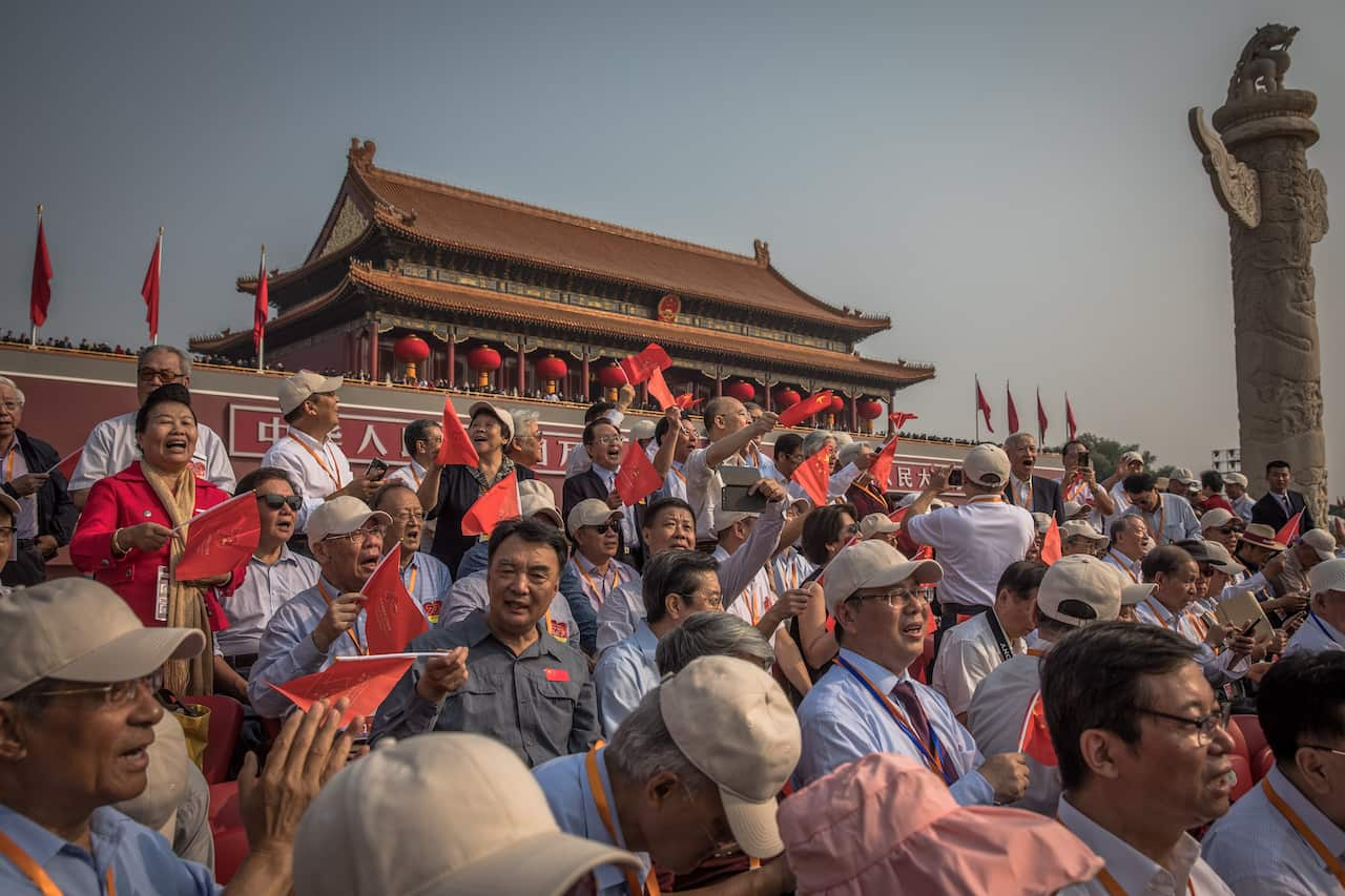 Visitors with Chinese flags sing as they wait for a military parade marking the 70th anniversary of the founding of the People's Republic of China, in Beijing