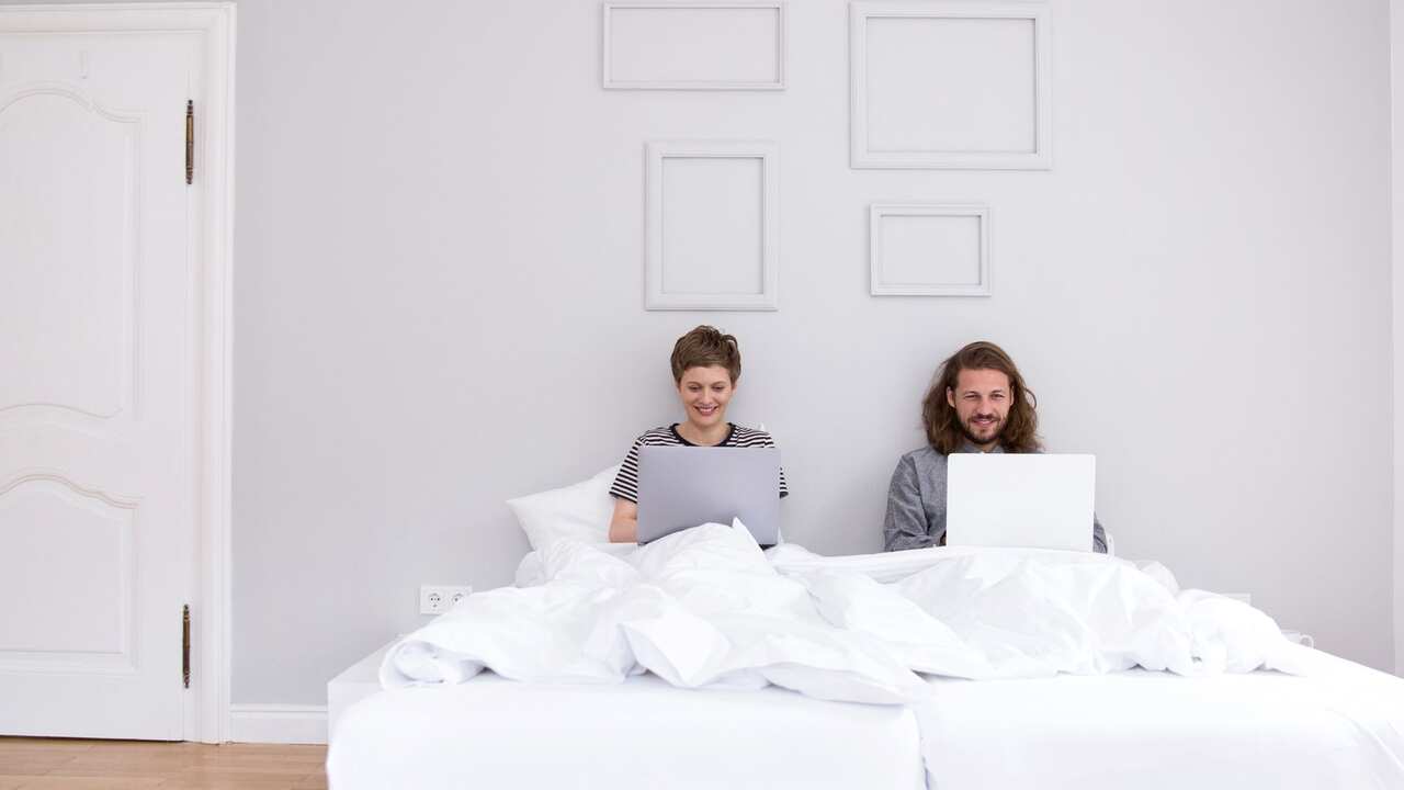 A man and a woman with laptops in their bed