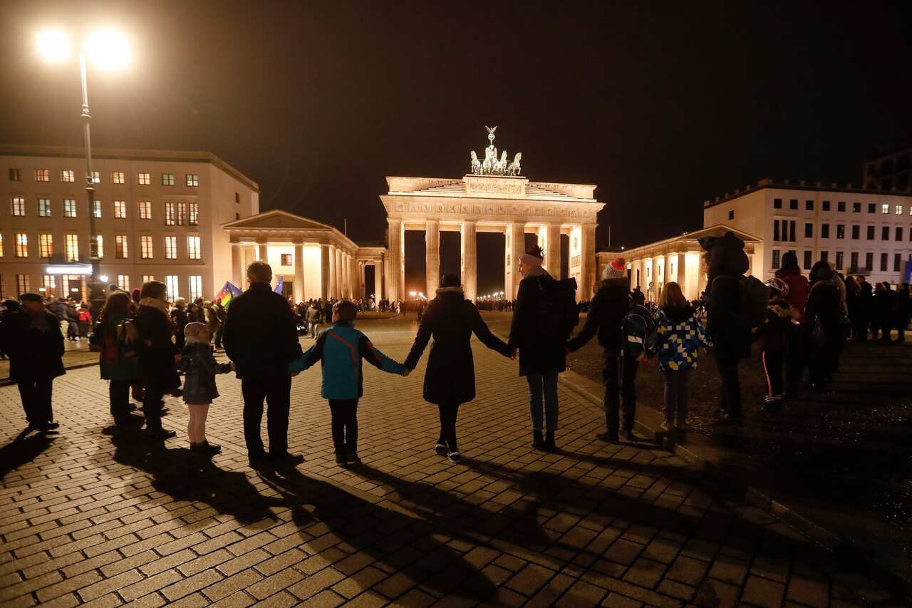 People stand for a human chain during a vigil for victims of last night's shooting in the central German town Hanau, in front of the Brandenburg Gate in Berlin.