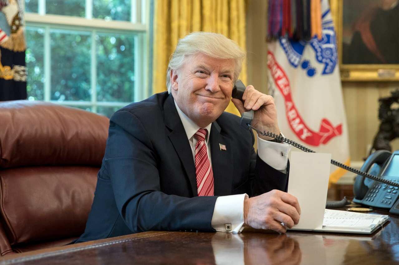 United States President Donald Trump holding a phone in the Oval Office.