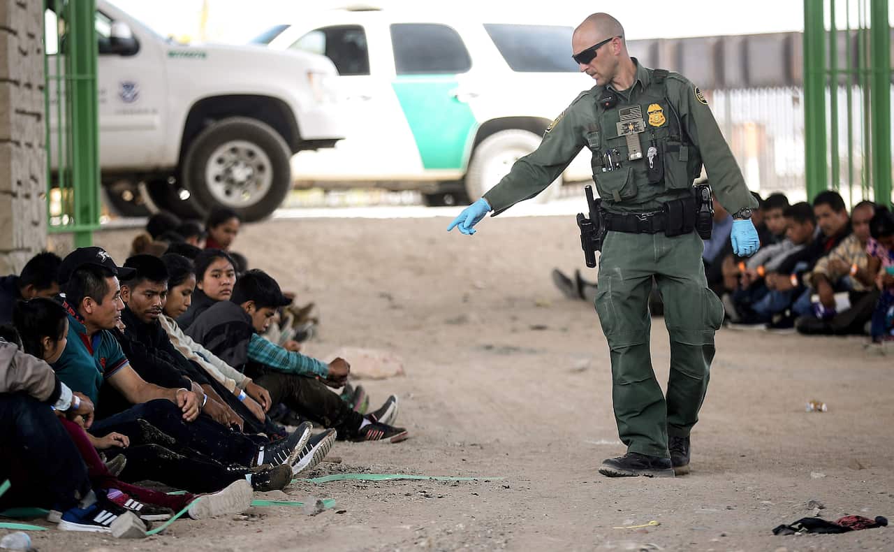 A US Border Patrol agent gestures towards migrants being detained after crossing to the US side of the US-Mexico border barrier.