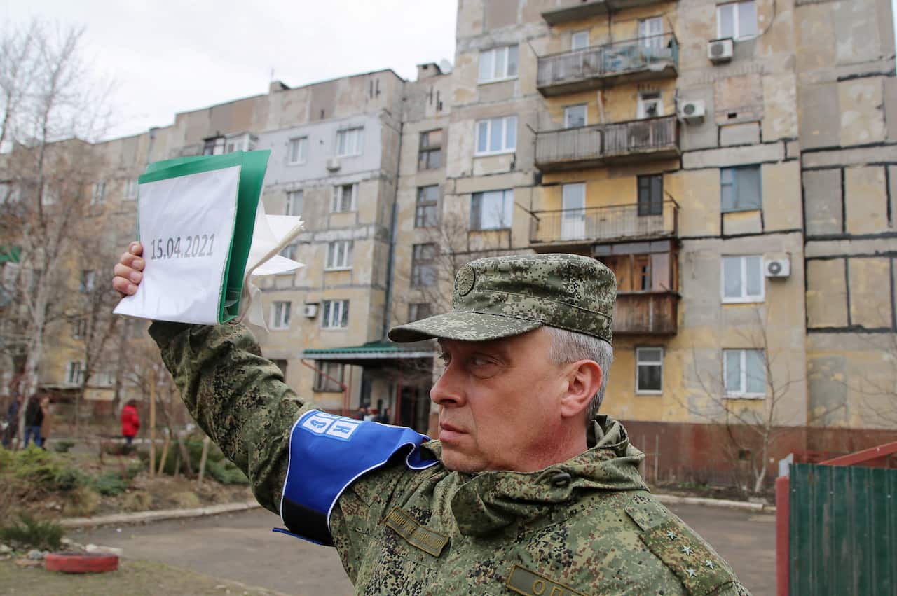 A representative of the Joint Center for Control and Coordination on ceasefire holds a sign by a house damaged in a shelling attack in Donetsk.