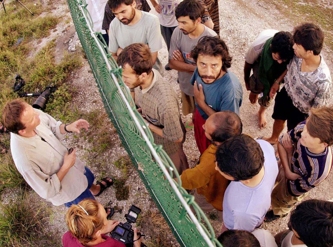 Refugees gather on one side of a fence to talk with international journalists about their journey that brought them to the Island of Nauru.