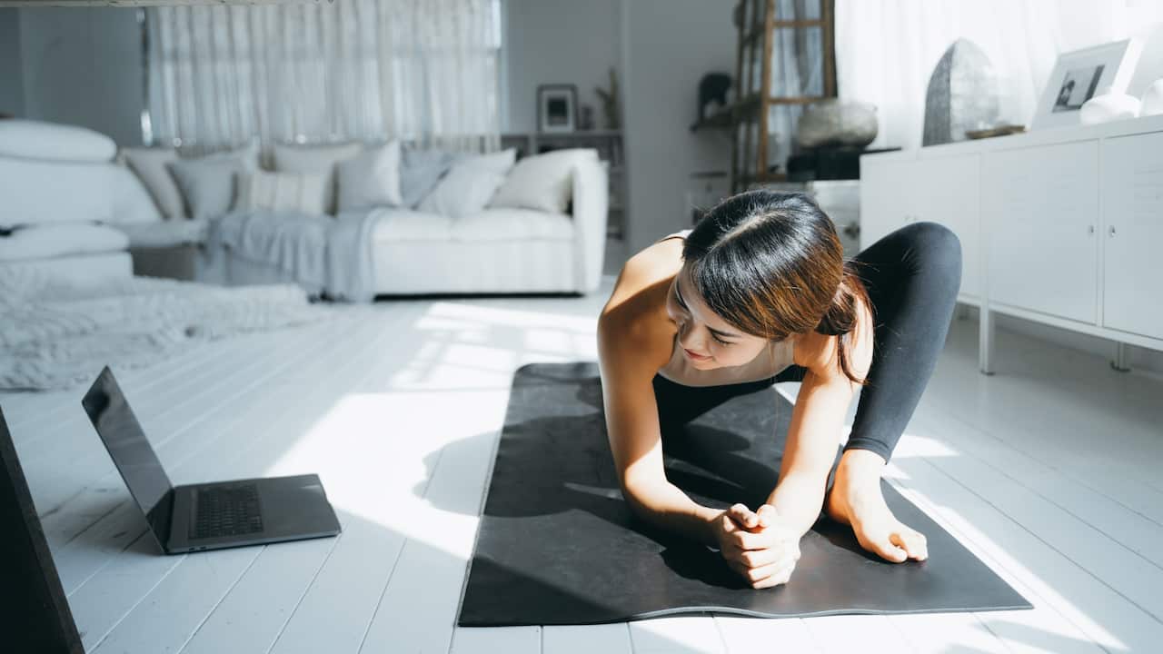 Young Asian woman doing online yoga class with laptop in the living room