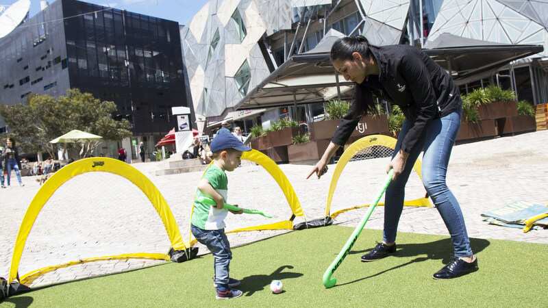 Penny Sidhu demonstrates Hockey to a kid at Fed Square