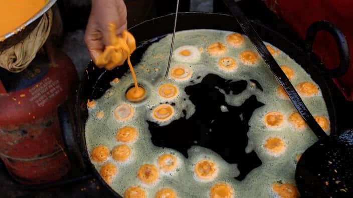 A worker prepares jalebi, a traditional Indian syrup-soaked pastry, at a streetside shop.