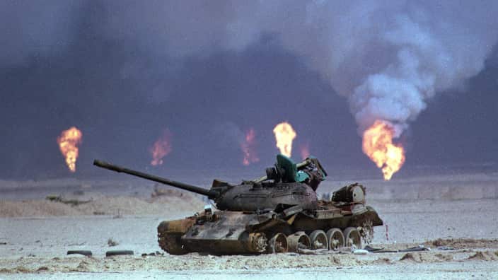 A destroyed Iraqi tank rests near a series of oil well fires during the Gulf War