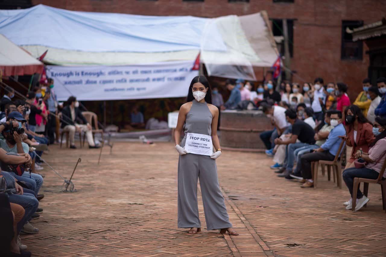 A model wearing a face mask with a placard catwalks during the protest in Kathmandu Nepal against what the protesters describe as government inaction in providing better covid-19 response.