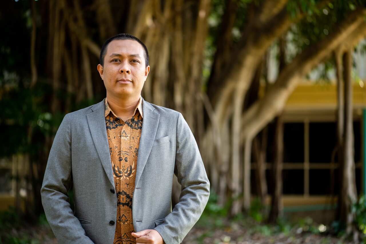 Mujiburrahman posing in the front of his office at Building Red 6, at the University of Charles Darwin