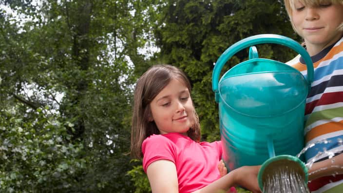 Boy and girl (7-9) watering garden together