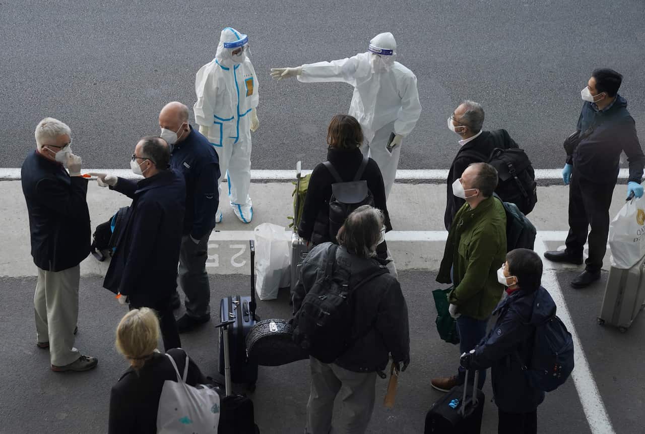 A worker in protective coverings directs members of the World Health Organization (WHO) team on their arrival at the airport in Wuhan in central China's Hubei province 