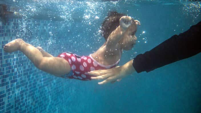 Wellbeing now. Young mothers. A mother submerges her child during a swimming lesson