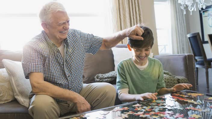Playful grandfather and grandson solving puzzle at home