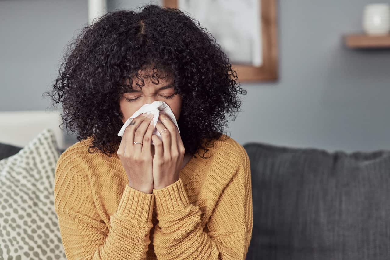 Shot of a young woman blowing her nose at home