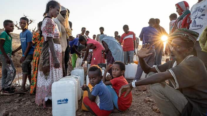 Tigray women and men who fled the conflict in Ethiopia's Tigray region, wait in line for water at a refugee camp.