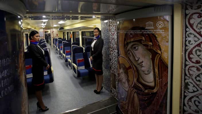 Train hostesses stand in a train carriage decorated with iconic religious figures as it departs from Belgrade to Mitrovica