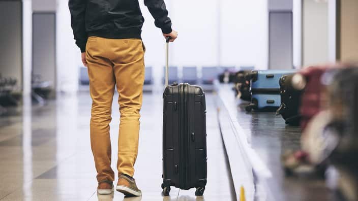 Low Section Of Young Man With Luggage Standing By Conveyor Belt At Airport
