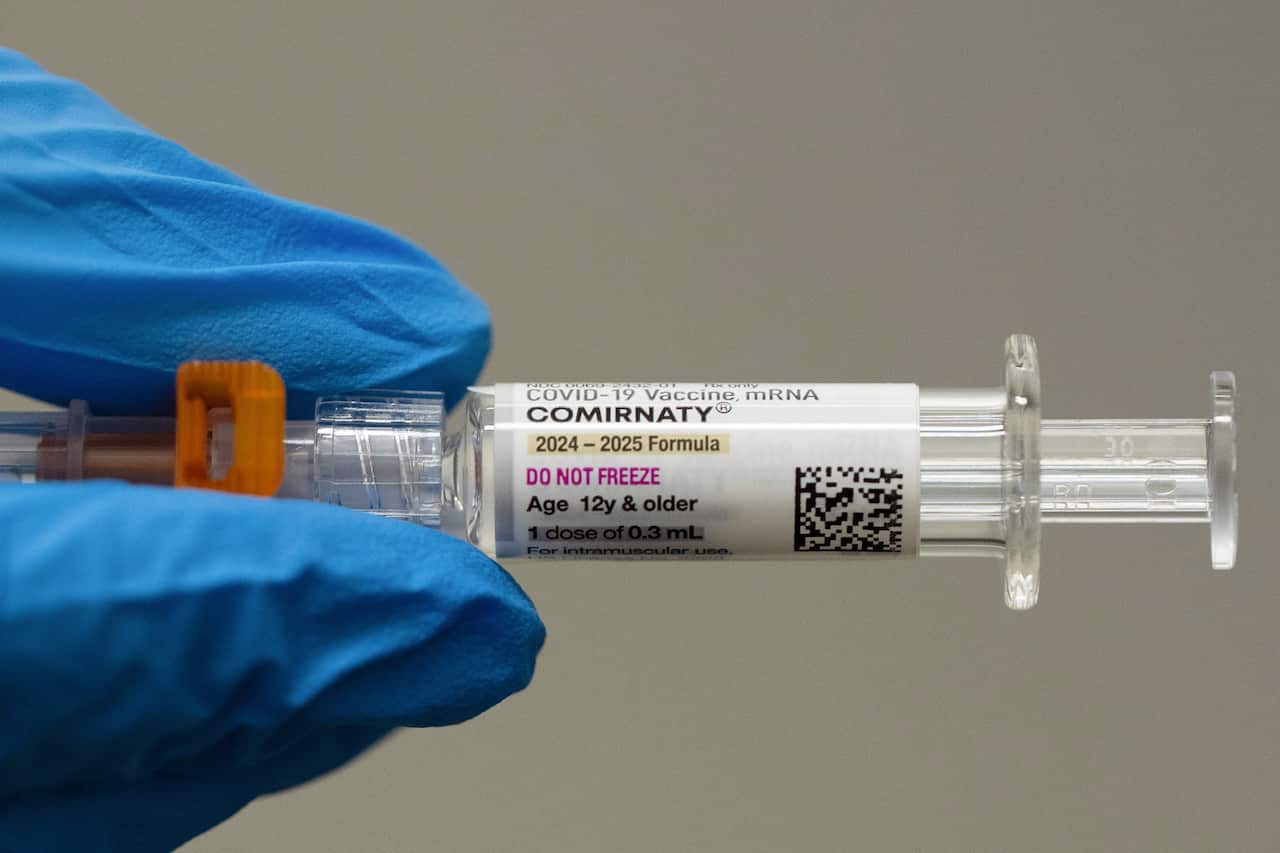 A blue glove on a hand holding a plastic syringe with writing on the label