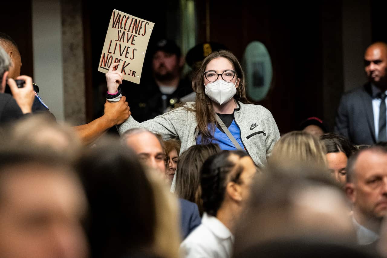 A protester holding a sign that says "Vaccines save lives no RKF Jr" is grabbed by the arm.