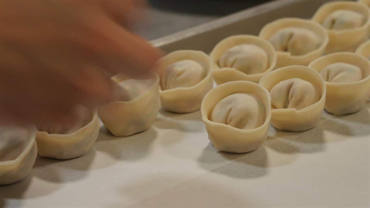 A close up on handmade dumplings lined up on a baking tray.