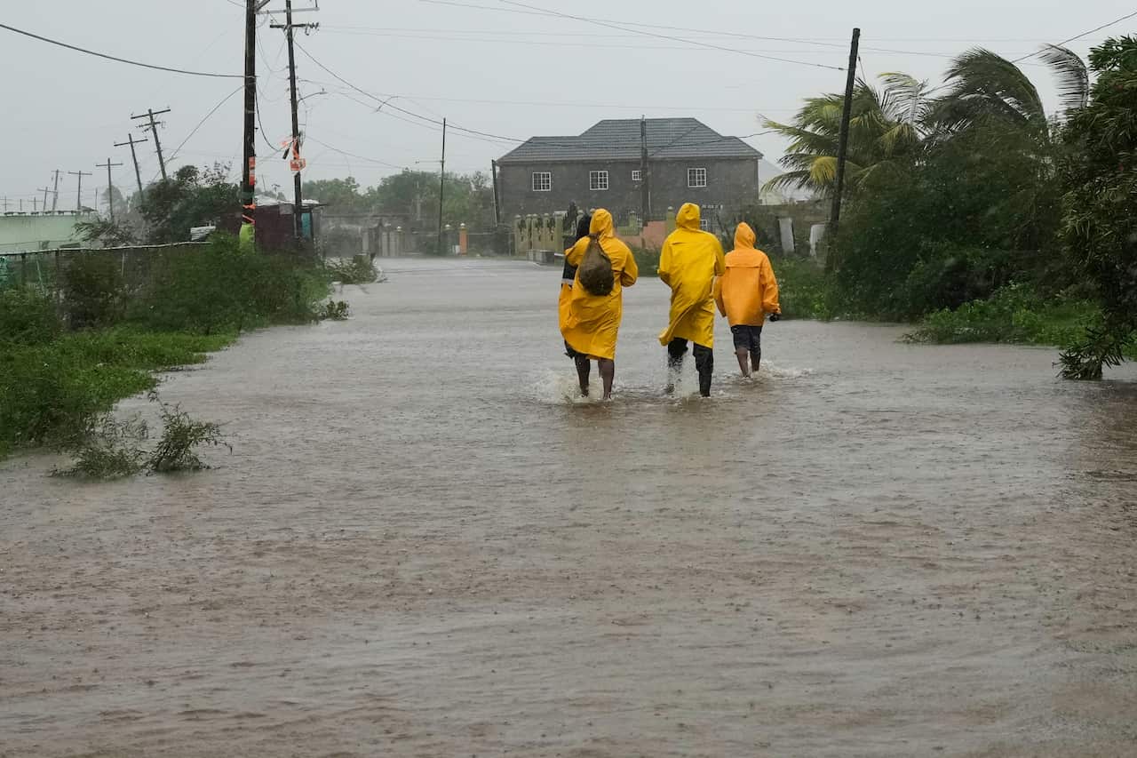 A group of three people in yellow raincoats walk across a flooded road with their backs turned.