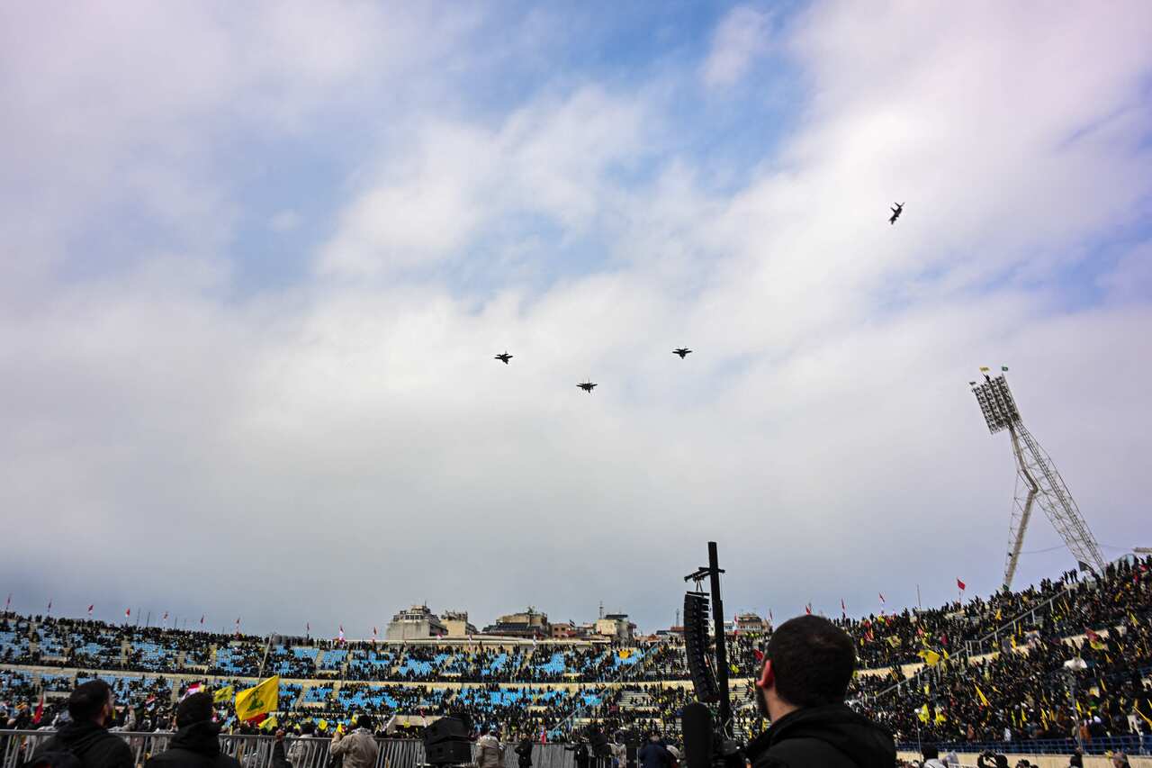 Fighter jets fly over a stadium full of people.