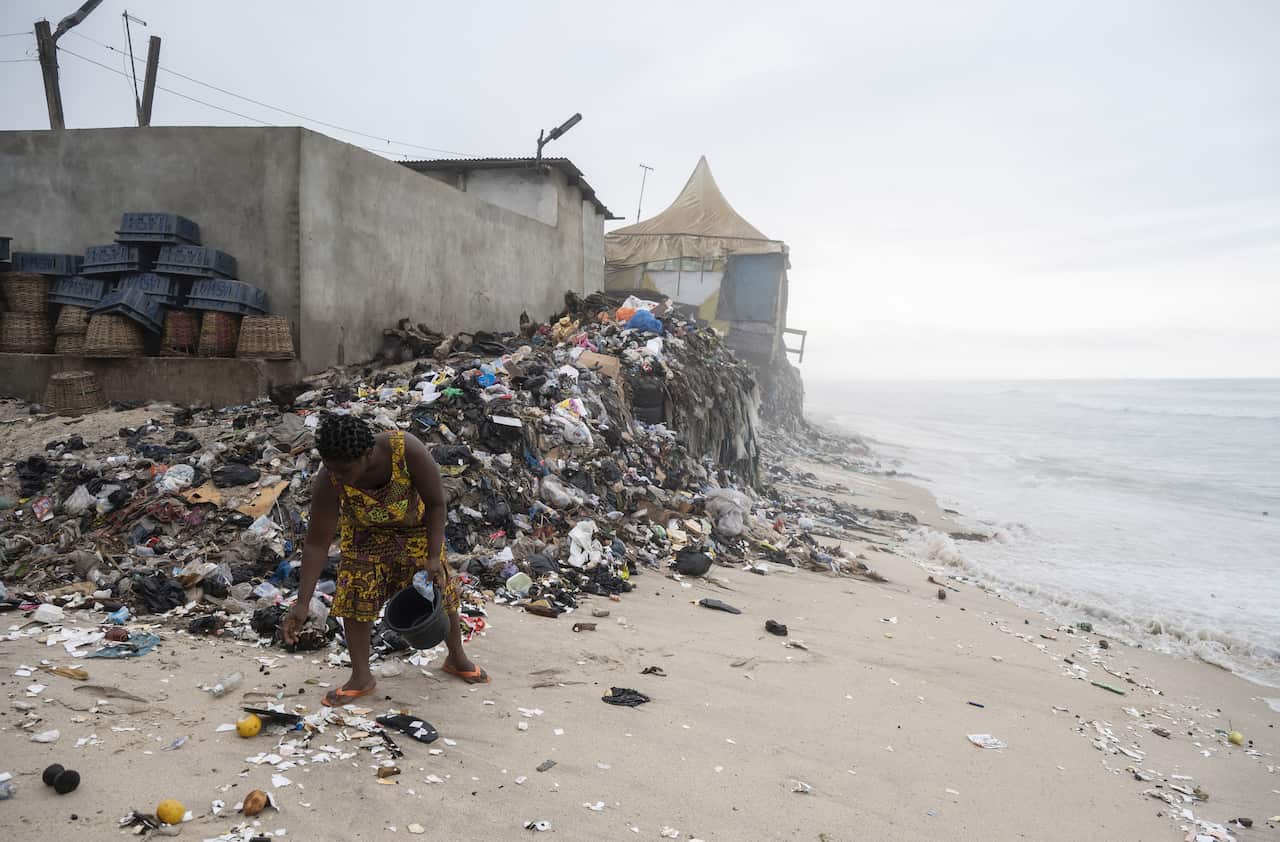 A beach in ghana is filled with trash as a young woman attempts to pick it up