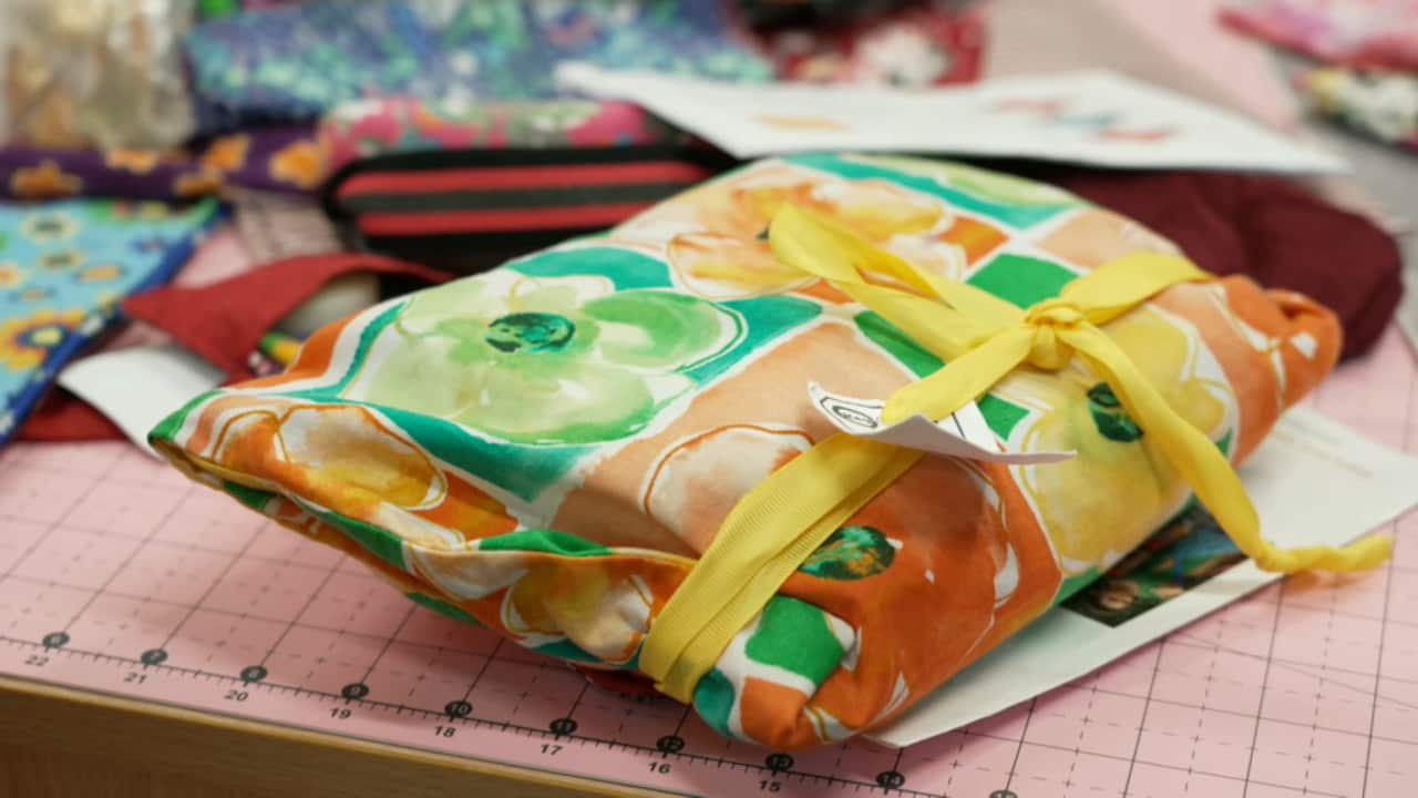 A drawstring bag made of orange, yellow and green fabric is tied up and sitting on a cutting mat.