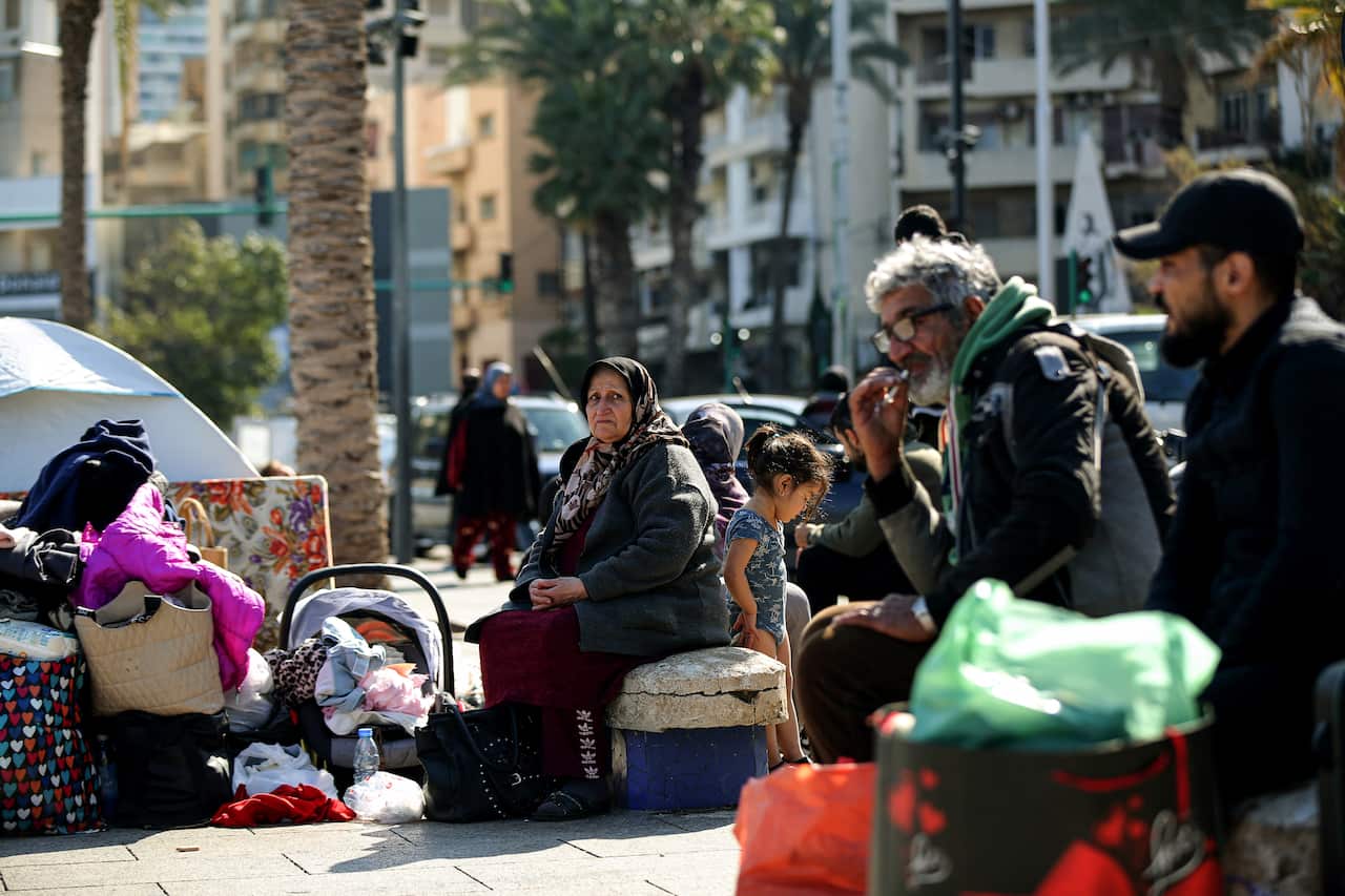 People sit among their belongings and luggage on the street