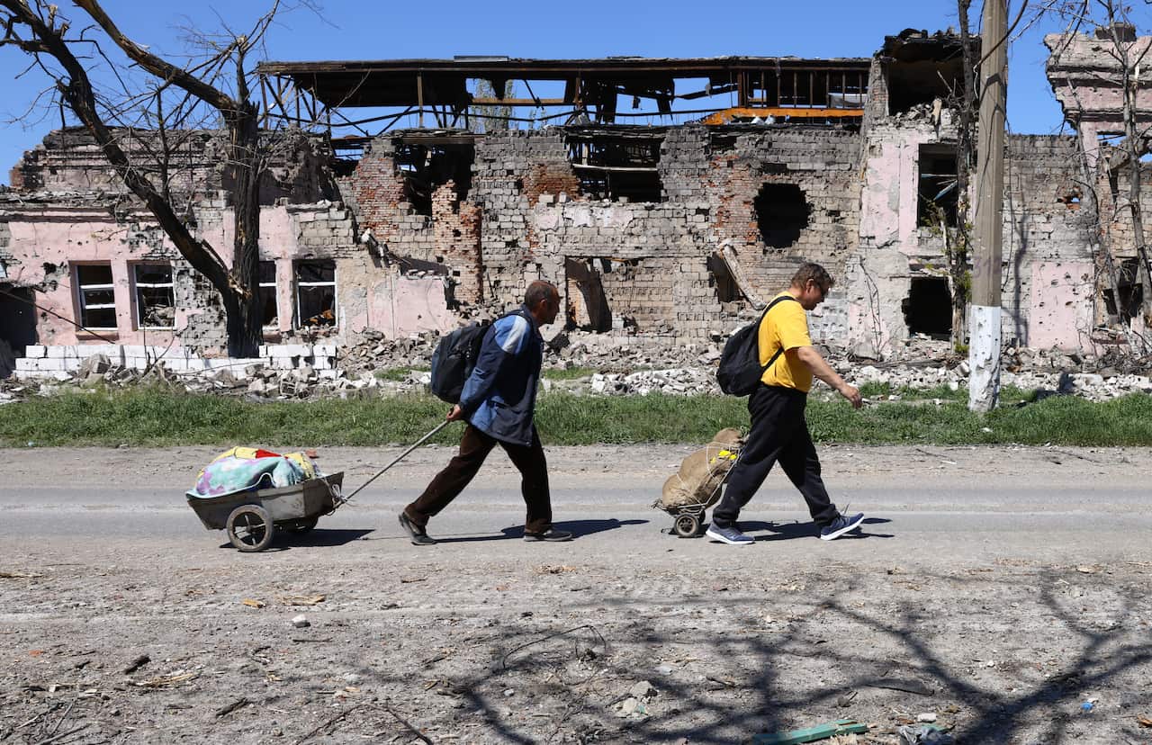 Local people walk past a damaged building in a street 