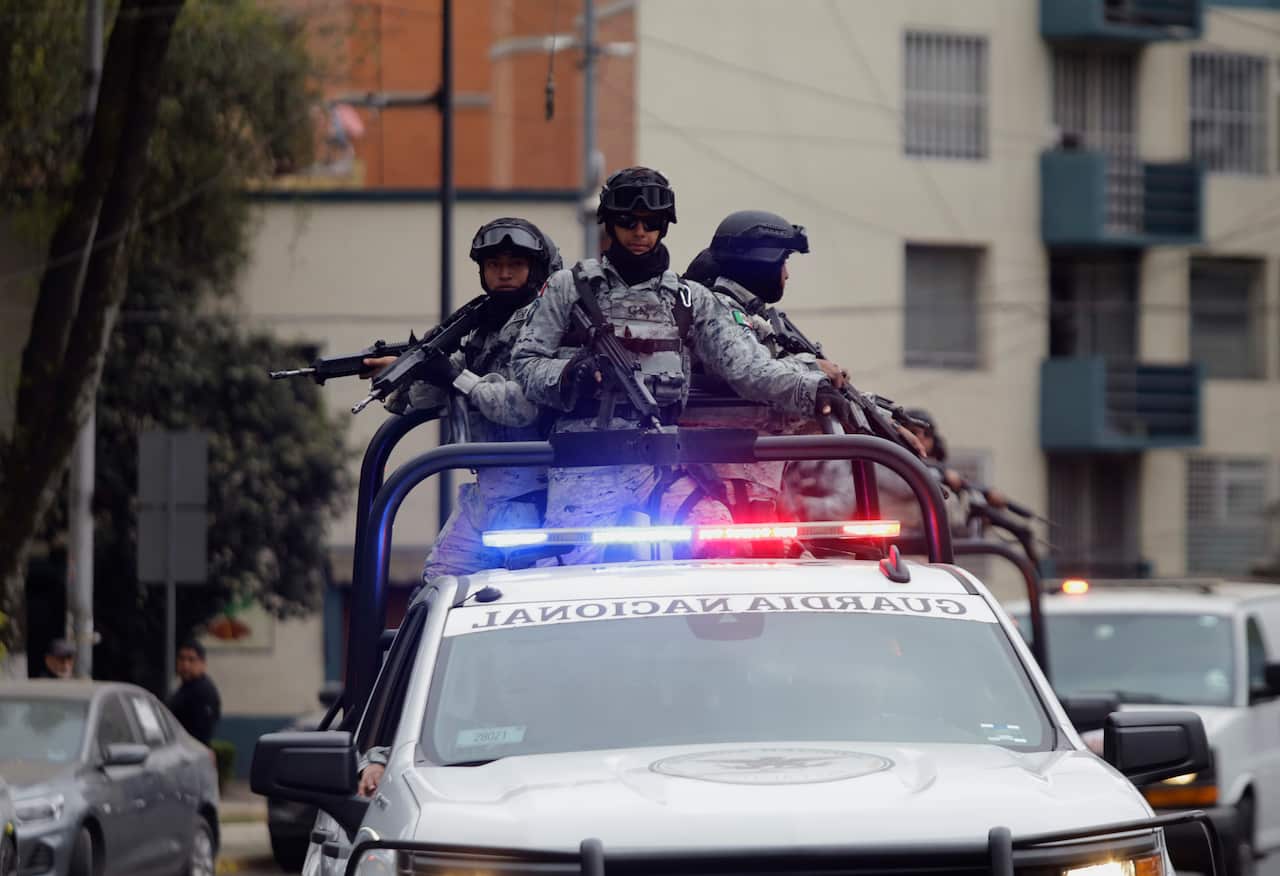 Members of the national guard stand with large guns in the back up a ute with its sirens flashing during an operation in Mexico City following the unrest.