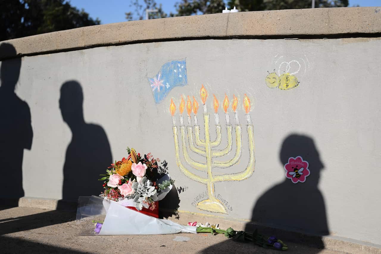 Drawings on a wall of a nine-branched candle holder, an Australian flag and a bee. A box of flowers is placed next to the scene.