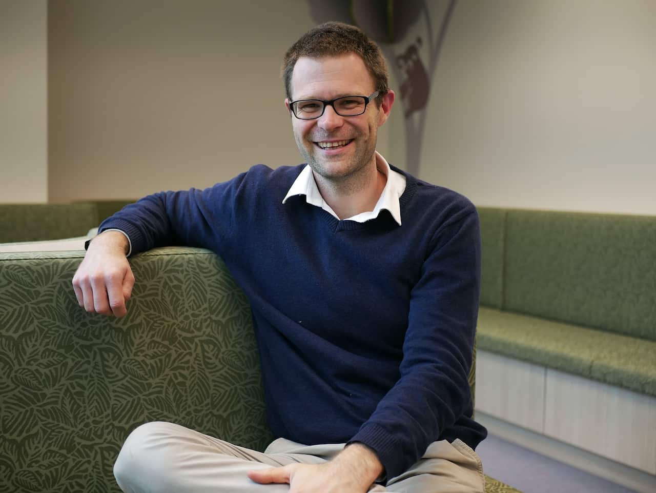 A smiling man, seated on a couch.