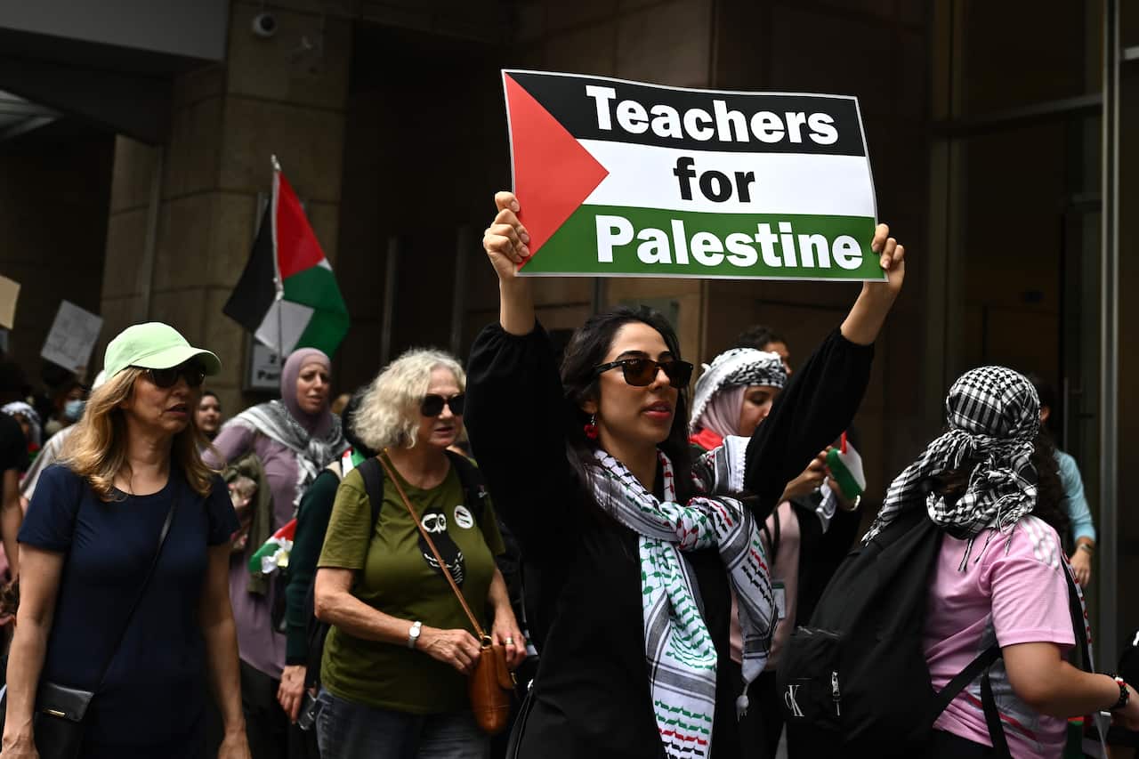 A woman holding a Palestinian flag reading "teachers for Palestine" at a protest.