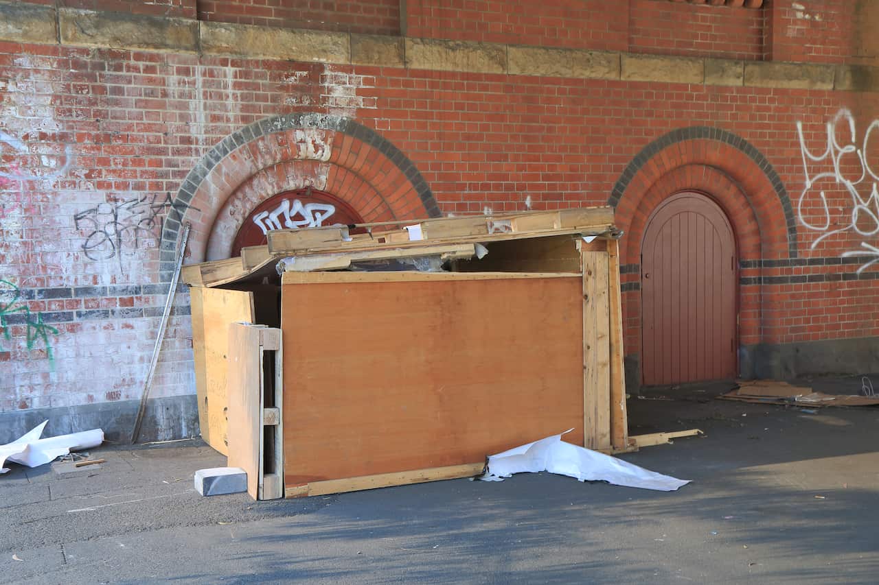 A makeshift shelter made from ply-board against a brickwall.