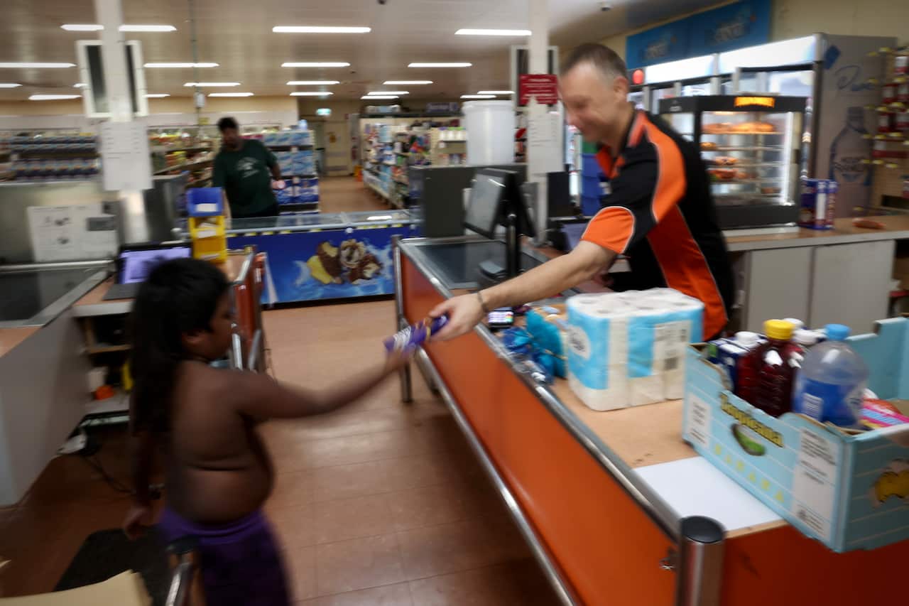 A child is handed a piece of chocolate by a cashier in a store.