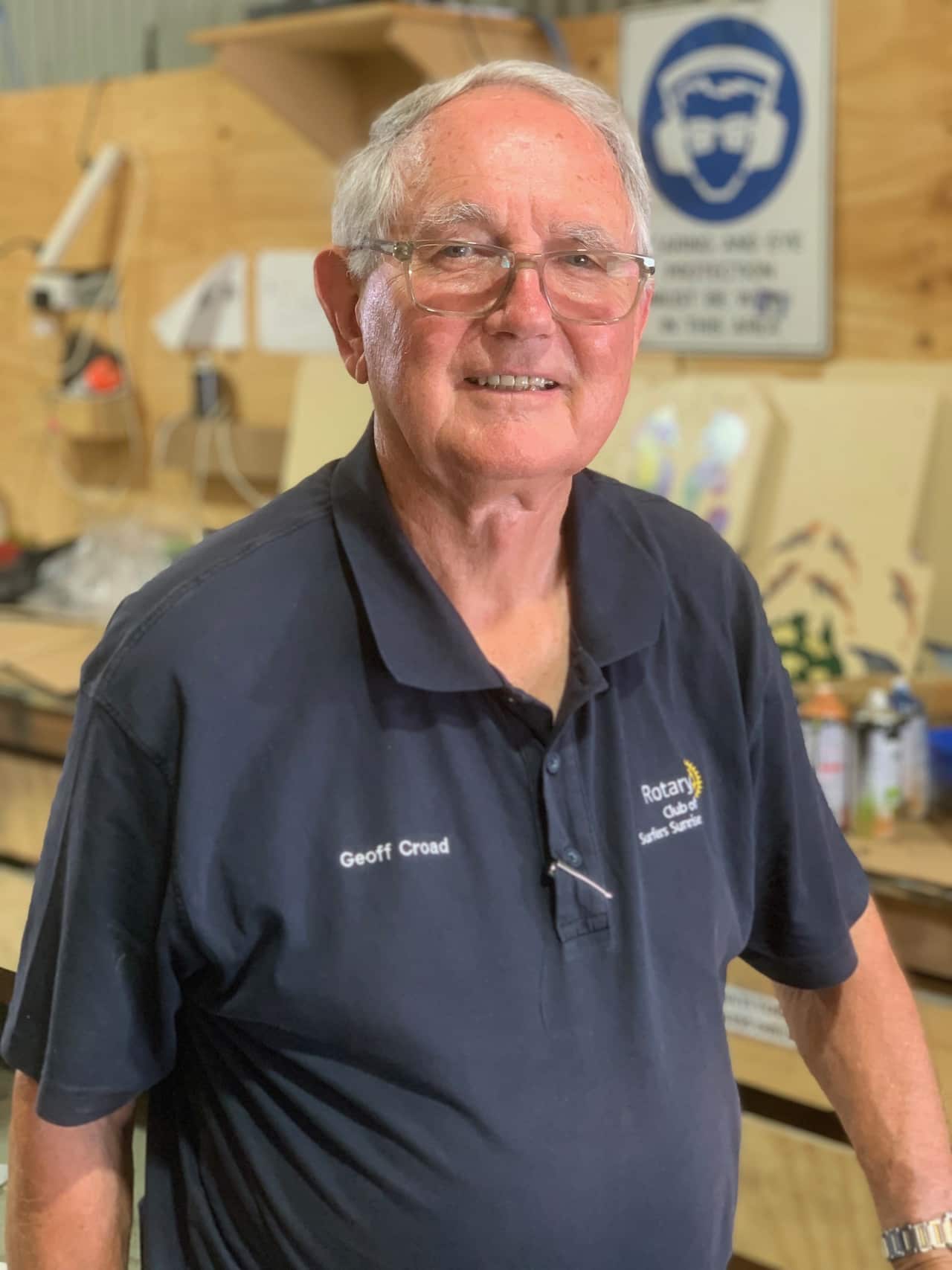 A man in a blue t-shirt stands smiling at camera.