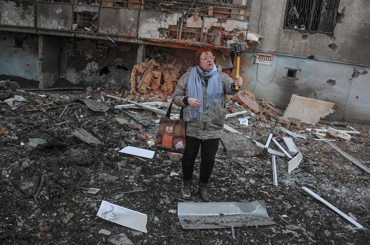 A woman stands next to a damaged building in the aftermath of shelling in Kharkiv.