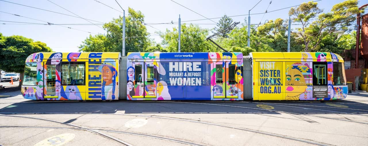 A picture of a tram passing by a road with SisterWorks' mission statement plastered on it in multiple colours.