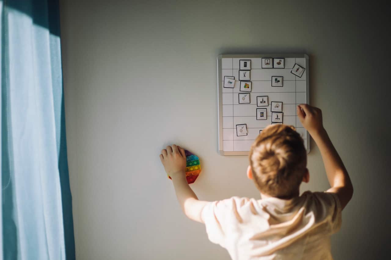 Rear view of boy going through weekly planner mounted on wall at home