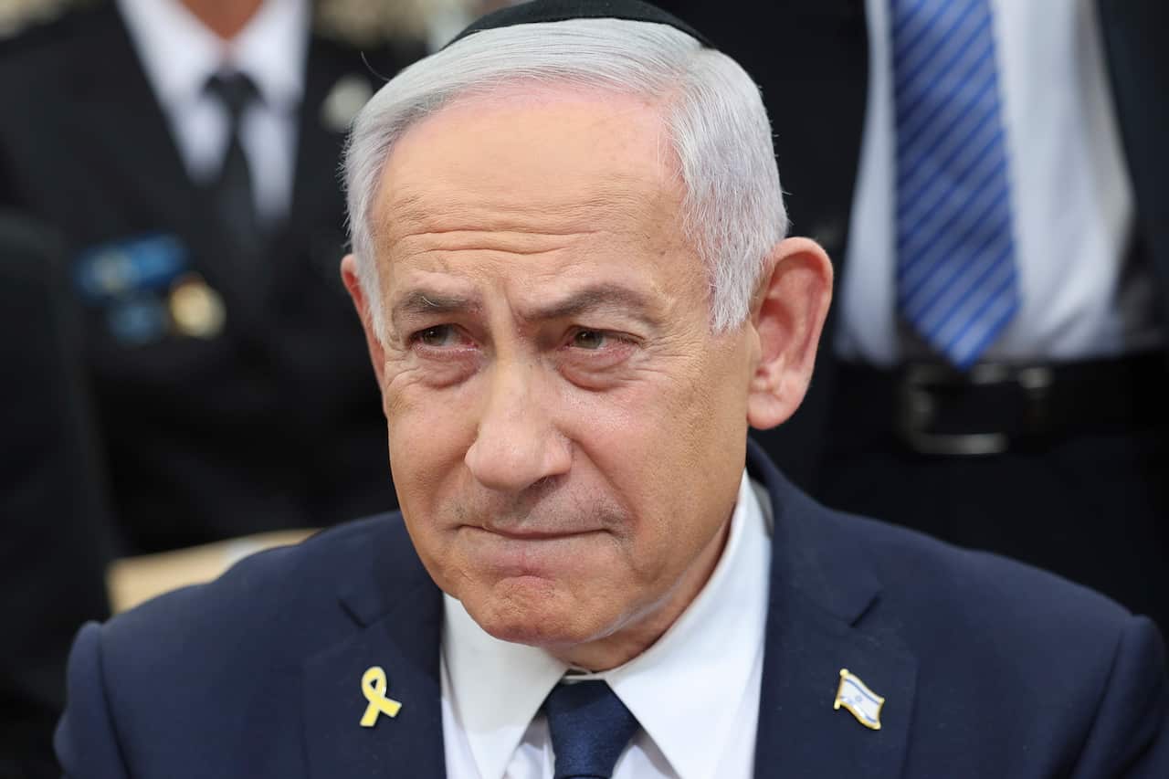 A close-up of a man wearing a white shirt, a blue suit, and two badges.