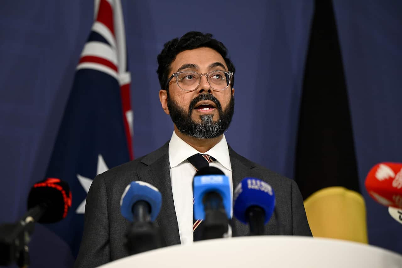 Man speaks at a podium with Australian and First Nations flags behind him