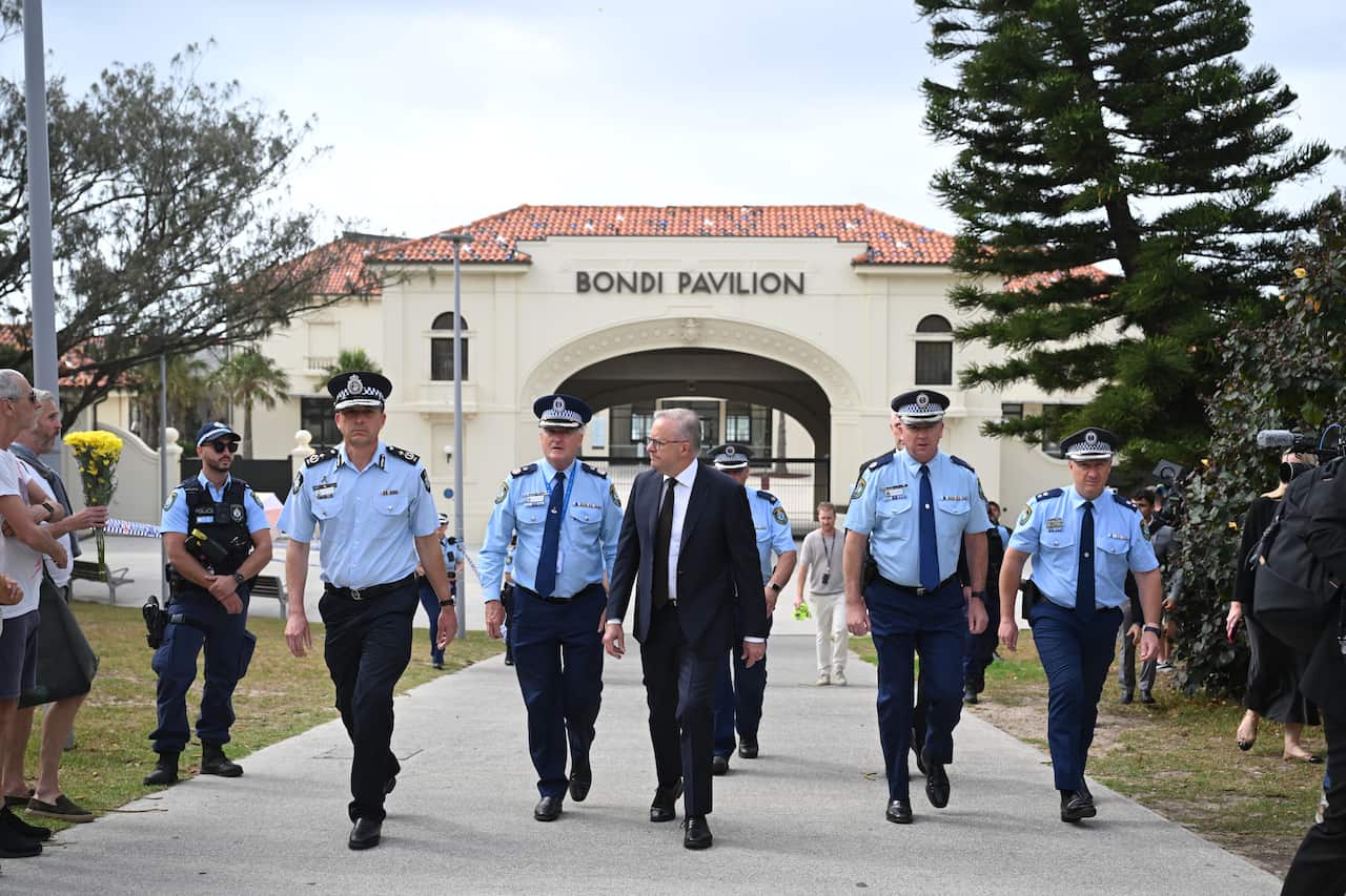Anthony Albanese, in a suit, walks with police officers around him.