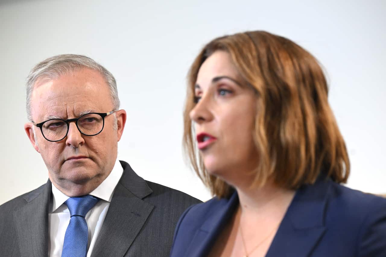 A woman speaks to someone off-screen while a man watches on.
