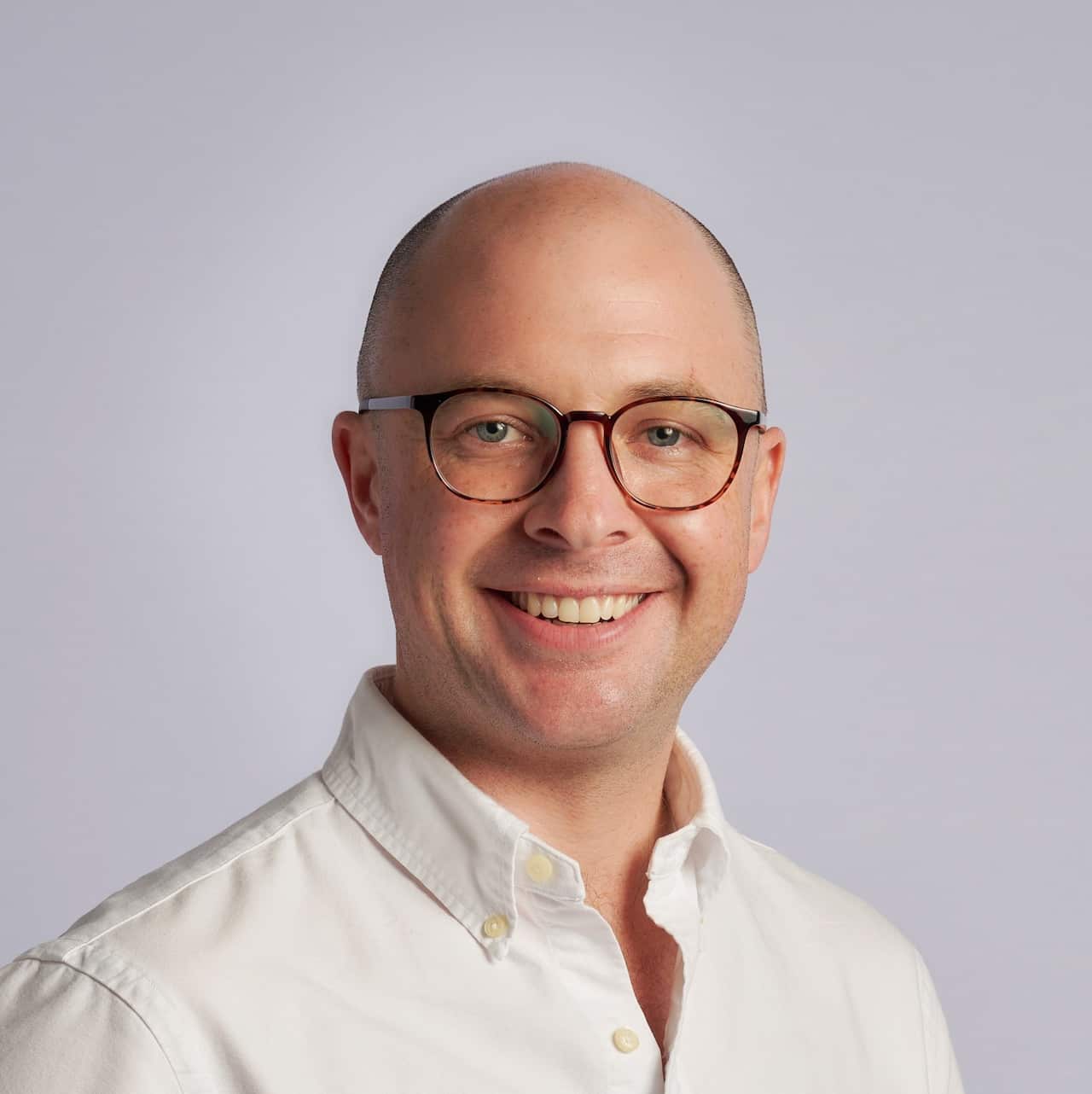 SA man wearing glasses and a white shirt smiles at camera.