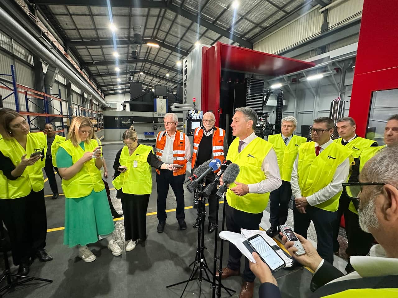 A group of people in high vis standing around for a media press conference.