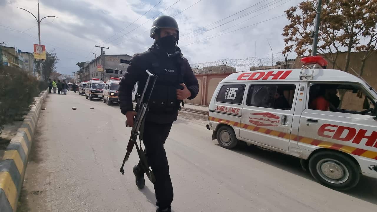 A policeman walks along a street carrying a gun.