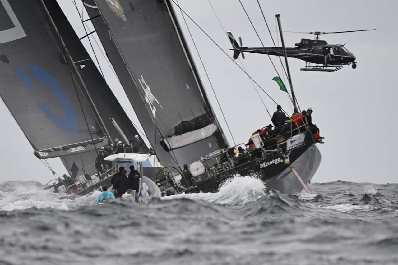 Un yate se inclina hacia un lado en aguas agitadas y un helicóptero sobrevuela.