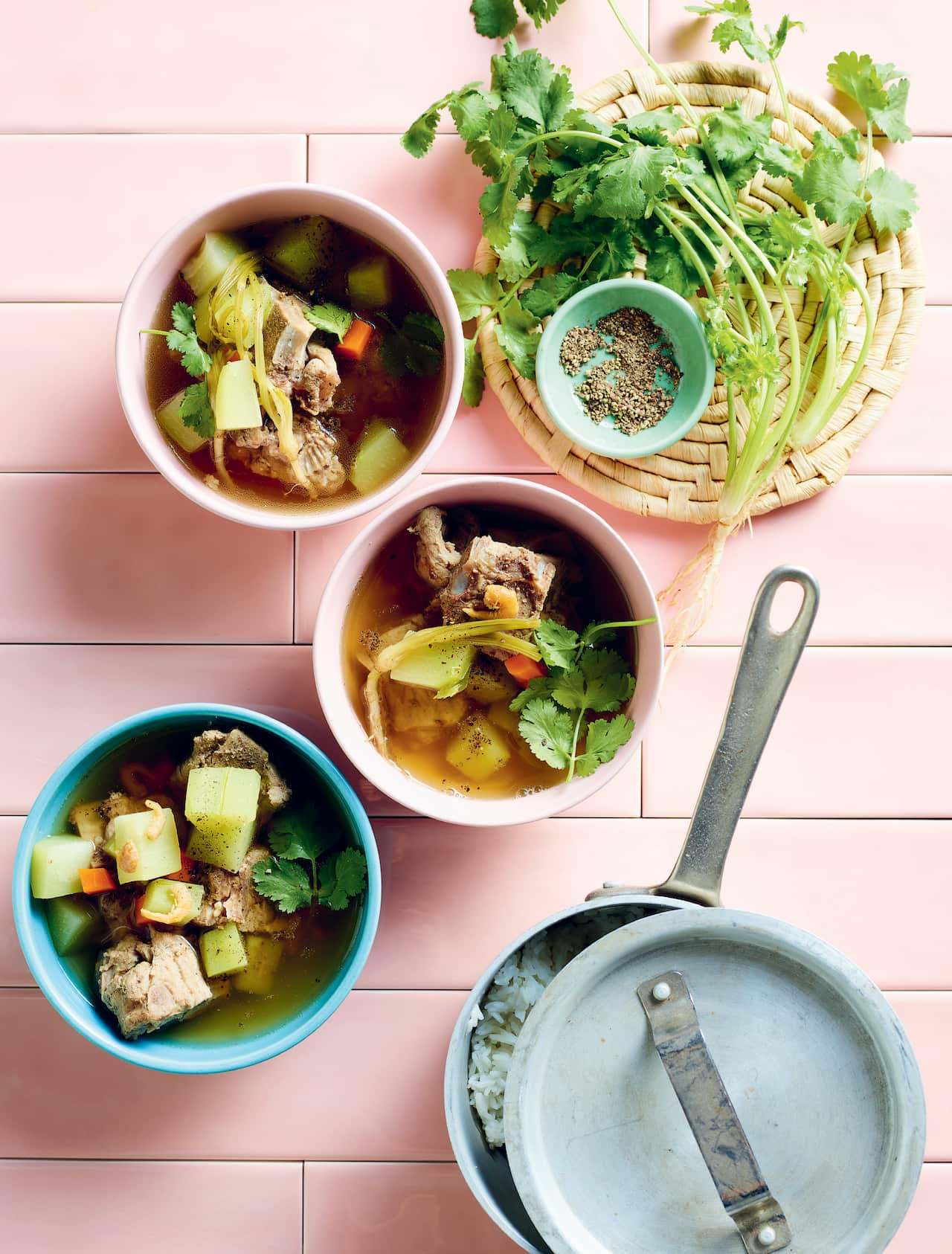 Vietnamese choko soup in bowls with meat, choko and other vegetables on pink tiles with coriander.